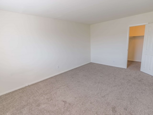 Spacious bedroom with grey carpeting, walk-in closet, and white walls.