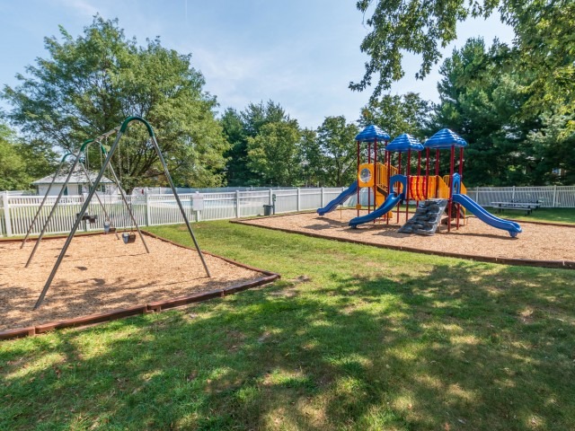 Playground area with slides and swing set on mulch and grass around it.