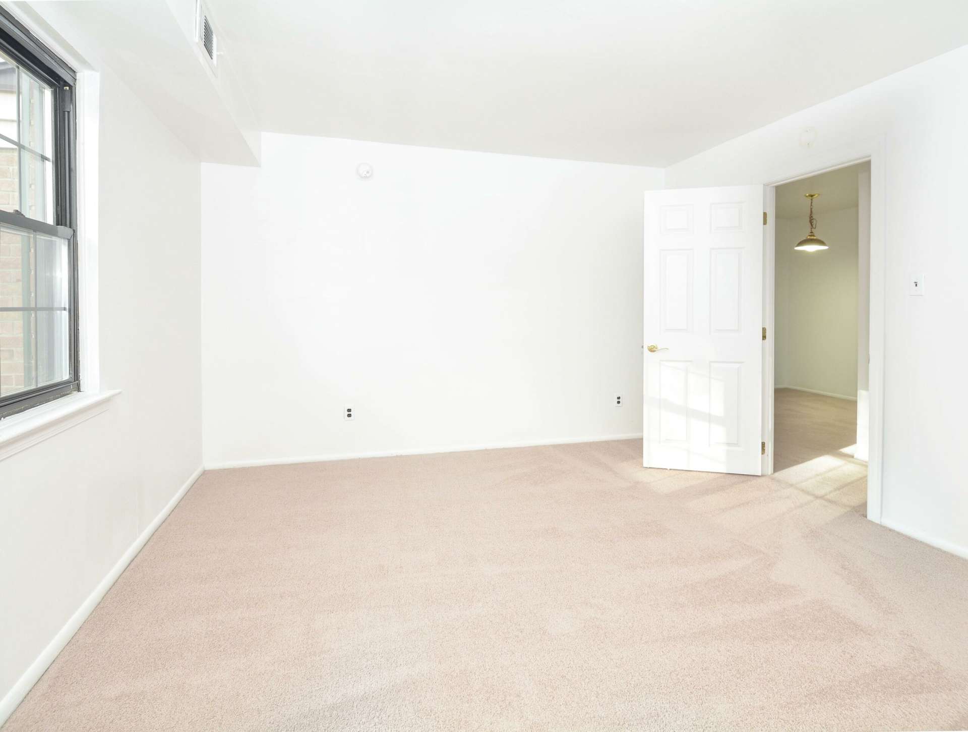 Spacious and carpeted bedroom with white walls and a window.