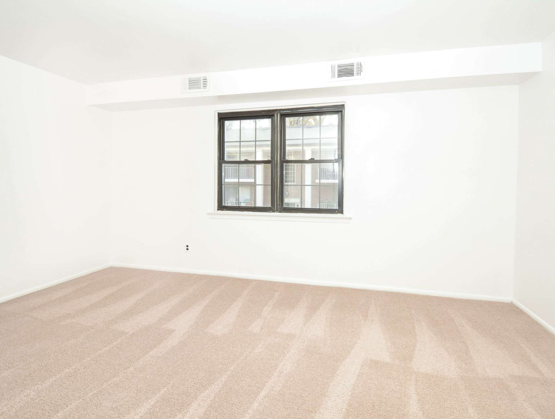 Bedroom with beige carpet, a window, and white walls in an apartment at Hillcrest Apartments.