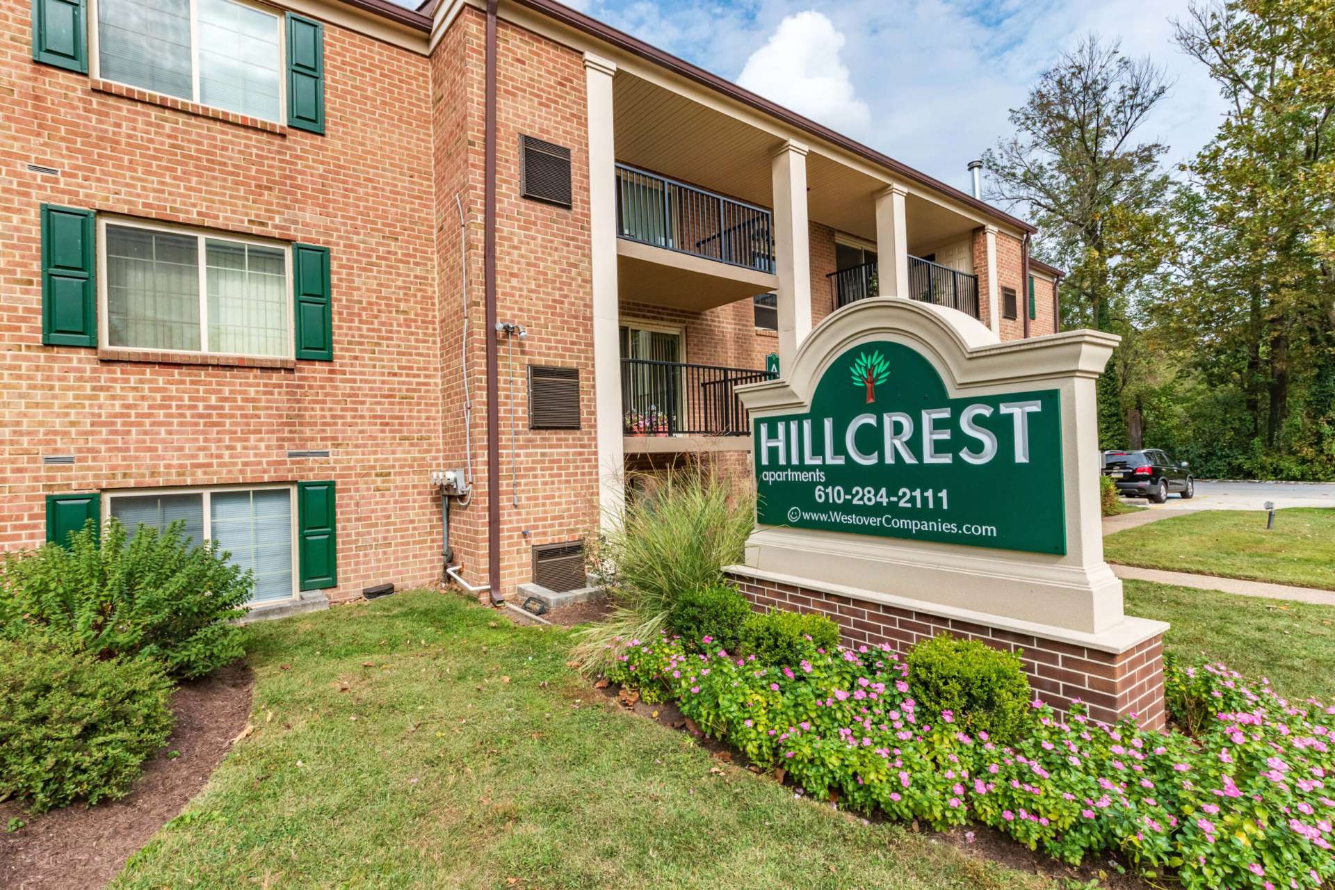 Hillcrest Apartments sign surrounded by flowers next to an apartment building.
