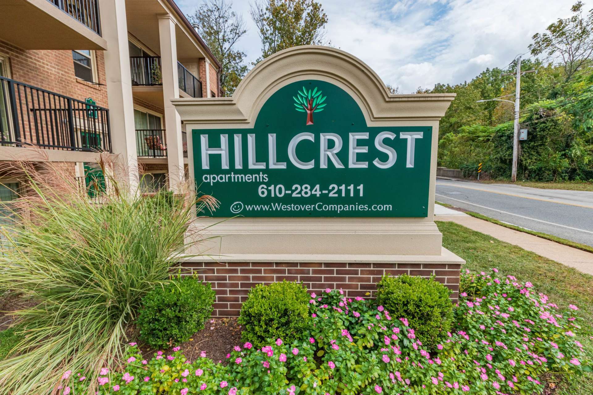 Hillcrest Apartments sign with pink flowers around the sign next to the road.