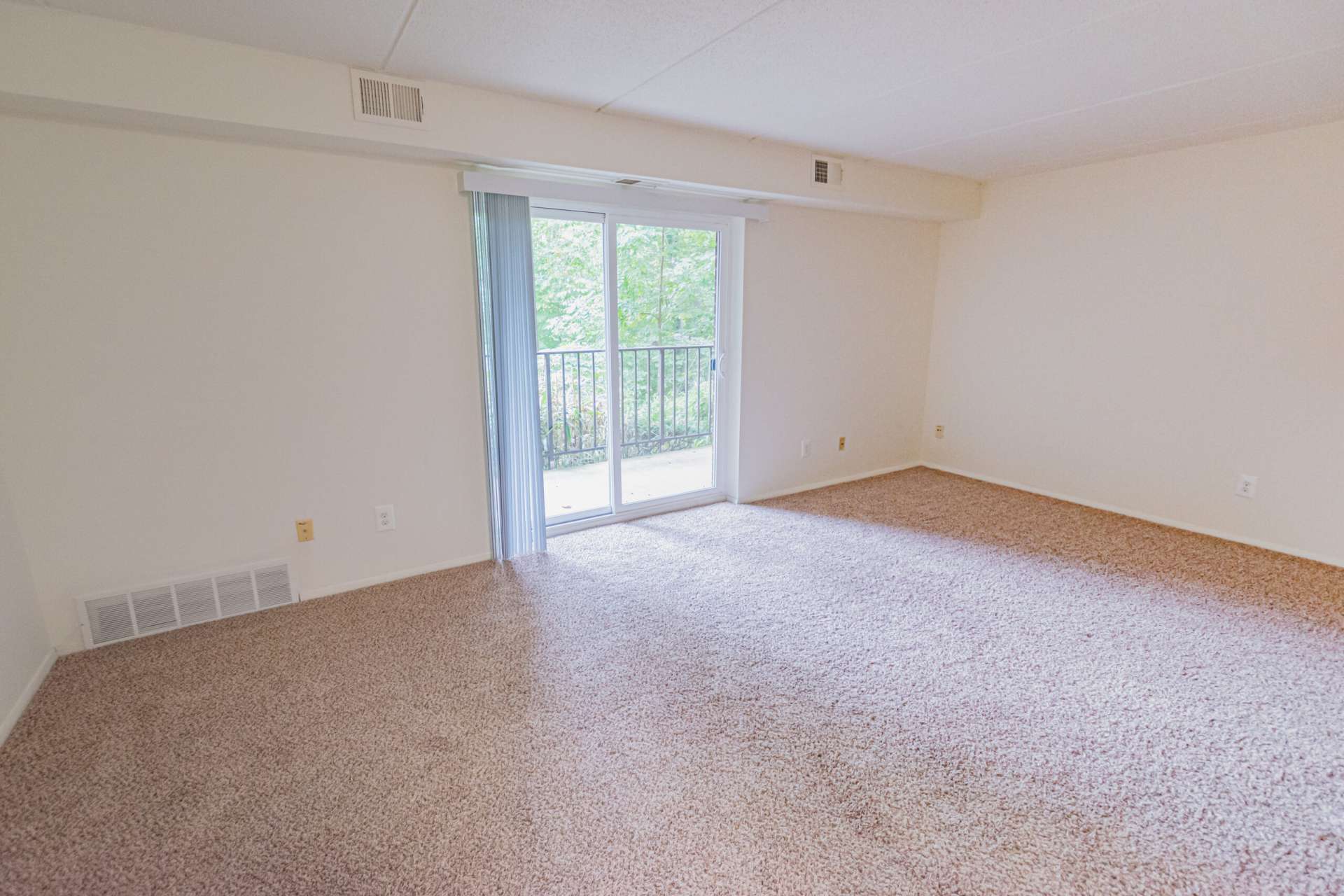 Spacious living room area with beige carpets and sliding glass doors that lead to the balcony.