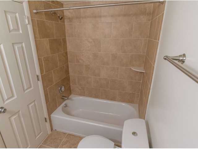 Bathroom with a bathtub, toilet, and light brown tiles.