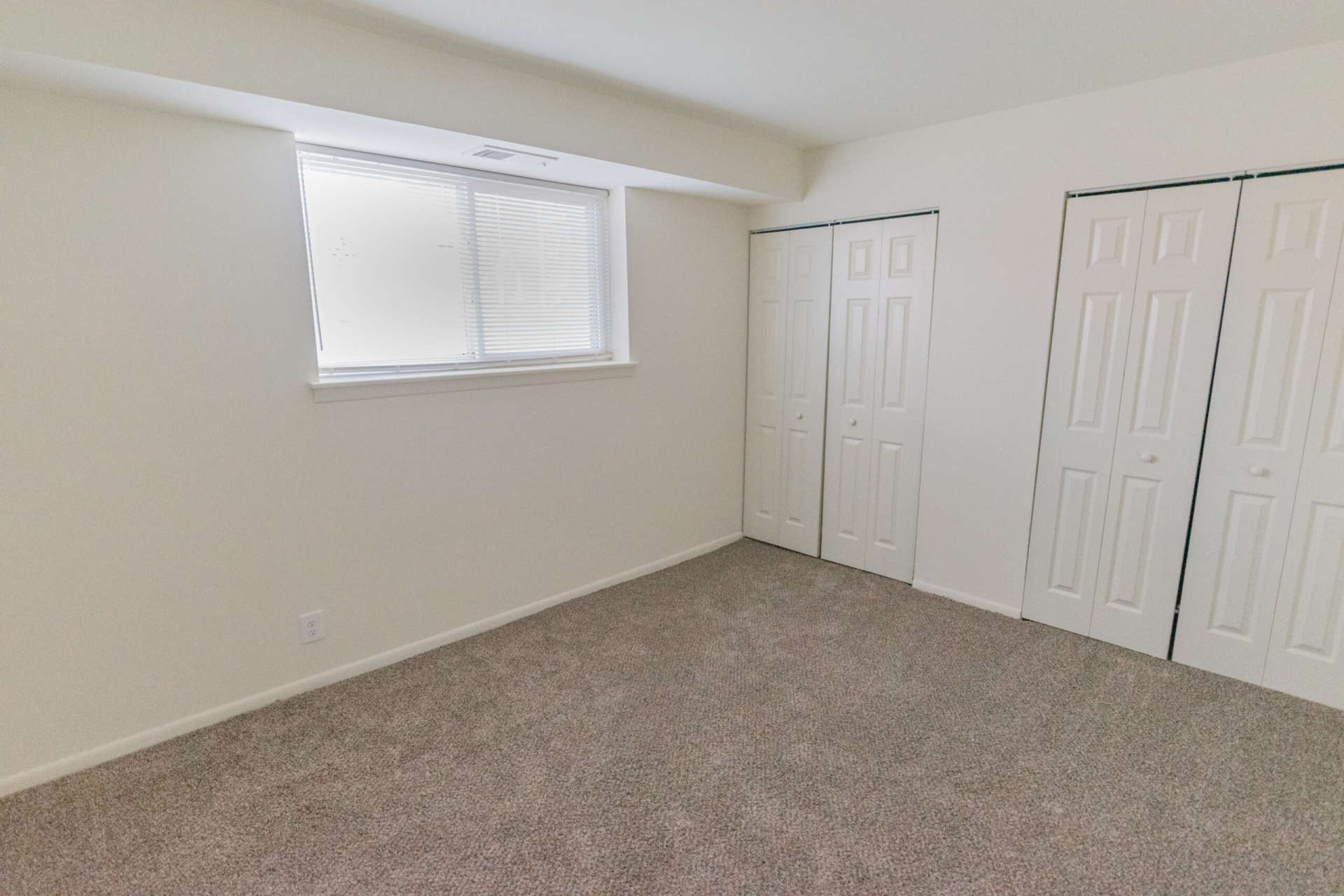 Bedroom with grey carpeting, window, and closet in an apartment at Jamestown Village.