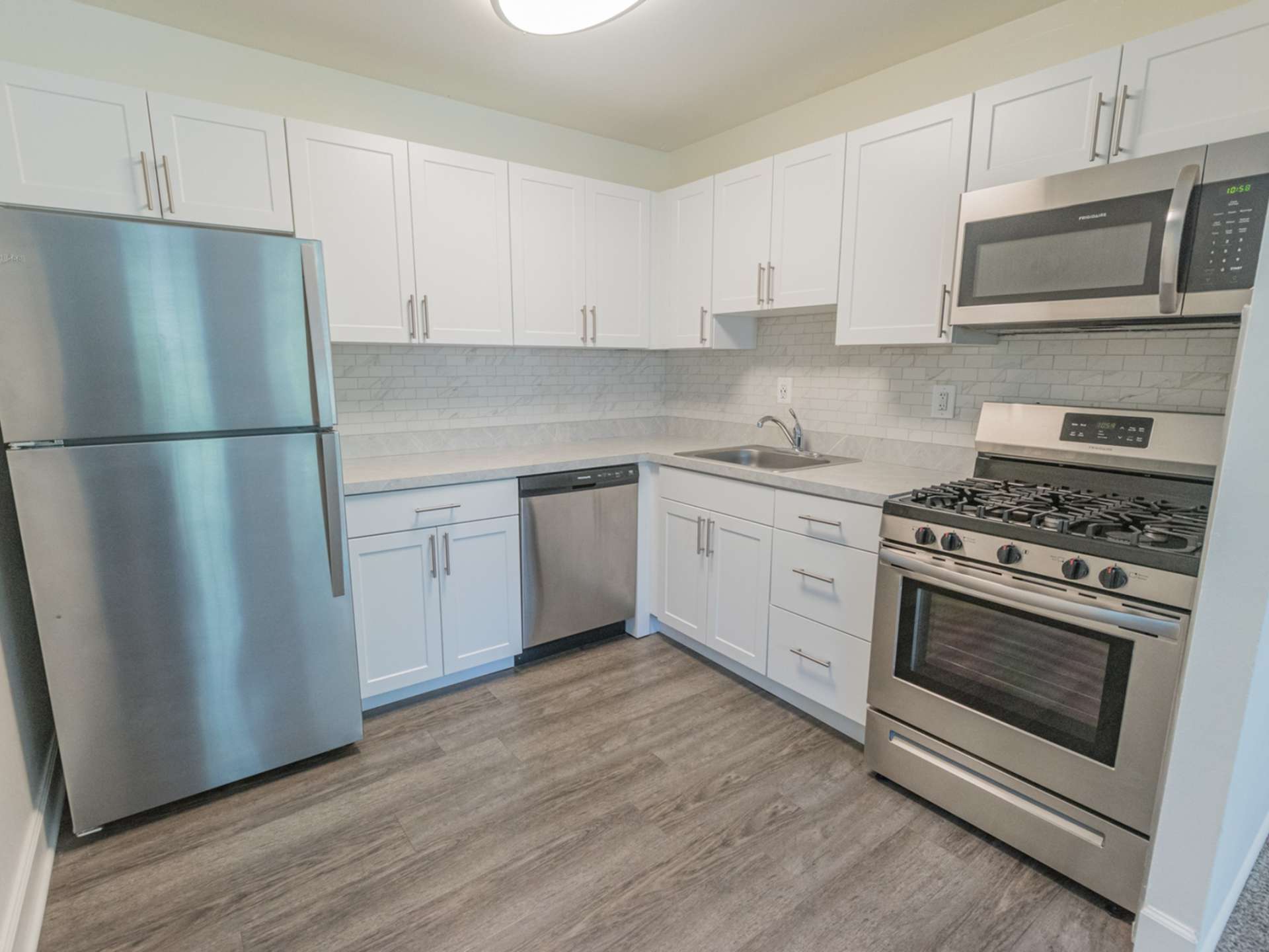 Kitchen with stainless steel appliances, white cabinets, and hardwood-style flooring.