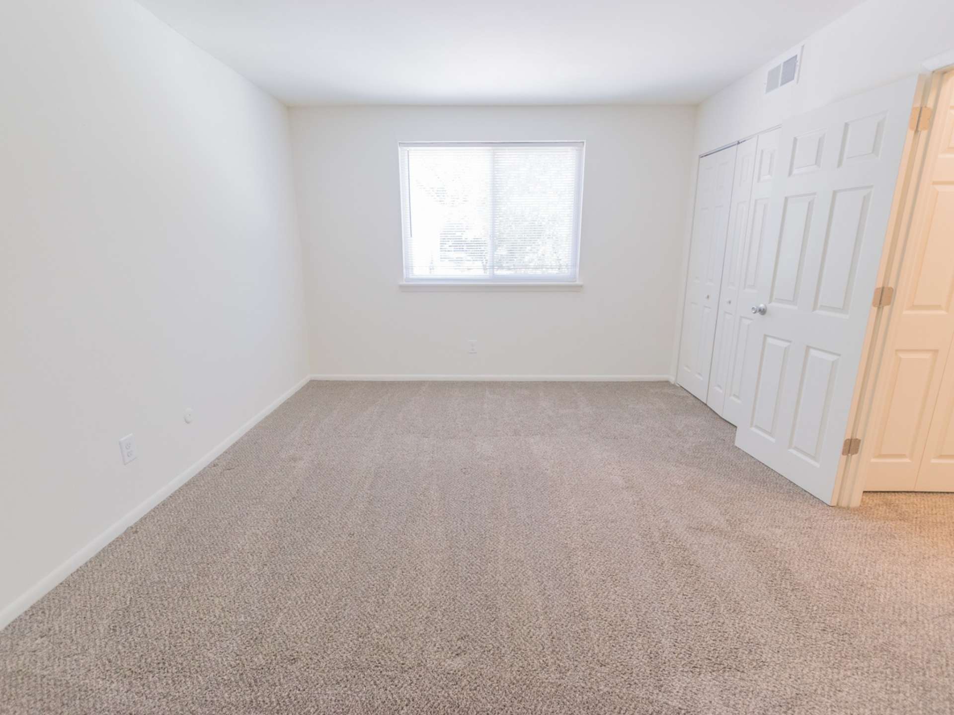 Carpeted bedroom with a large window, white walls, and closet.