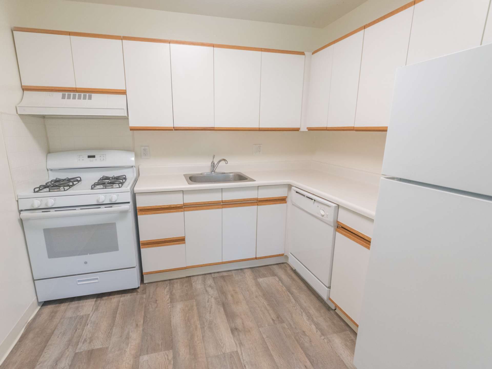 Kitchen with dishwasher, stovetop oven, fridge, and hardwood-style floors.