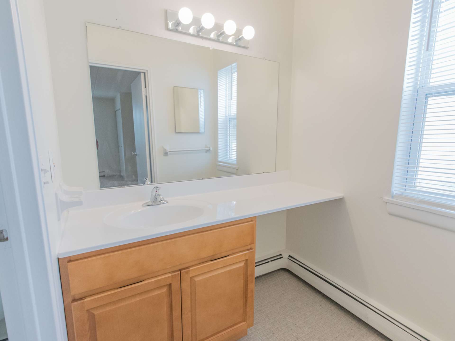 A bathroom with a large mirror, a window, and vanity lights.