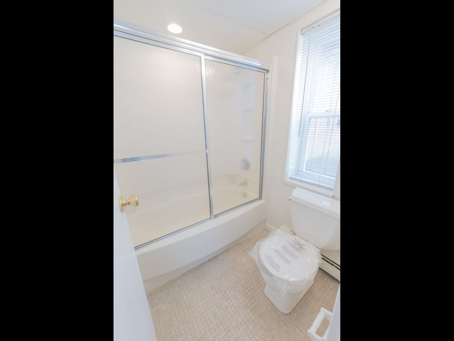 Bathroom with a toilet and bathtub shower with sliding glass doors.