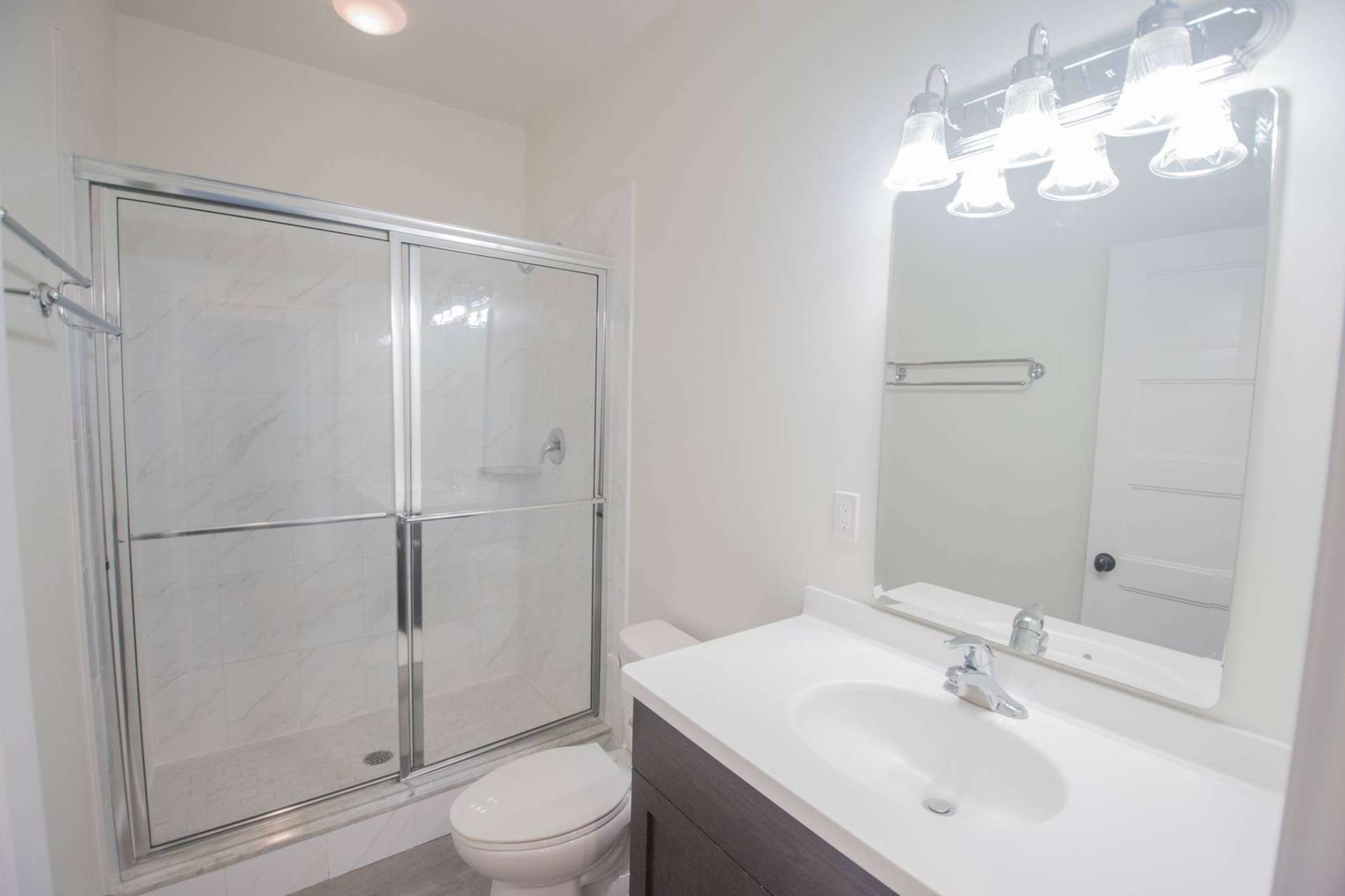Bathroom with vanity lights, a large mirror, and a sliding glass door to the shower.