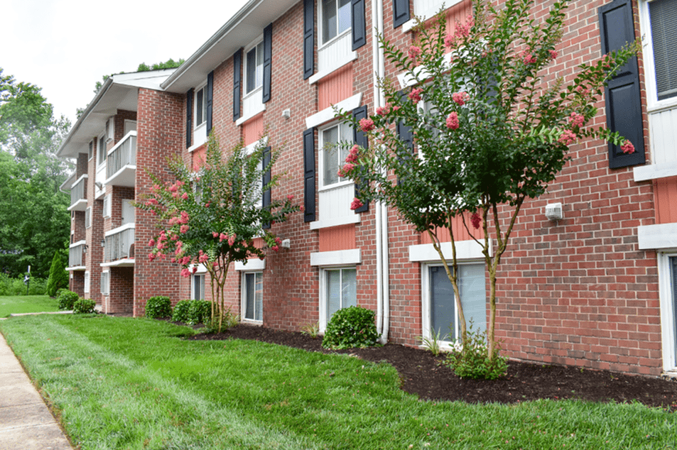 Exterior of an apartment building at fitted with a paved walkway, a garden, and a lawn