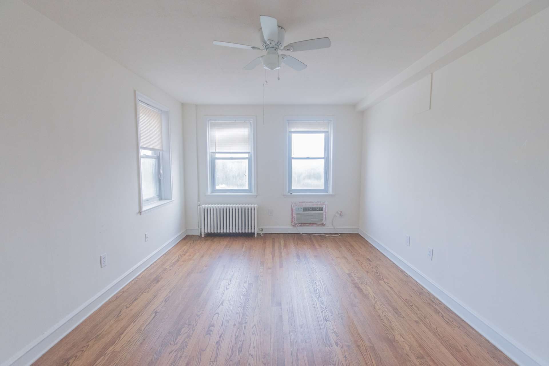 Living room area of an apartment unfurnished, fitted with vinyl flooring, a ceiling fan, and huge windows