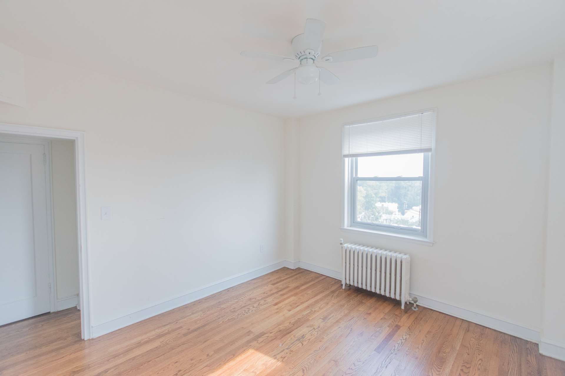 Living room area of an apartment unfurnished, fitted with vinyl flooring, a ceiling fan, and a radiator