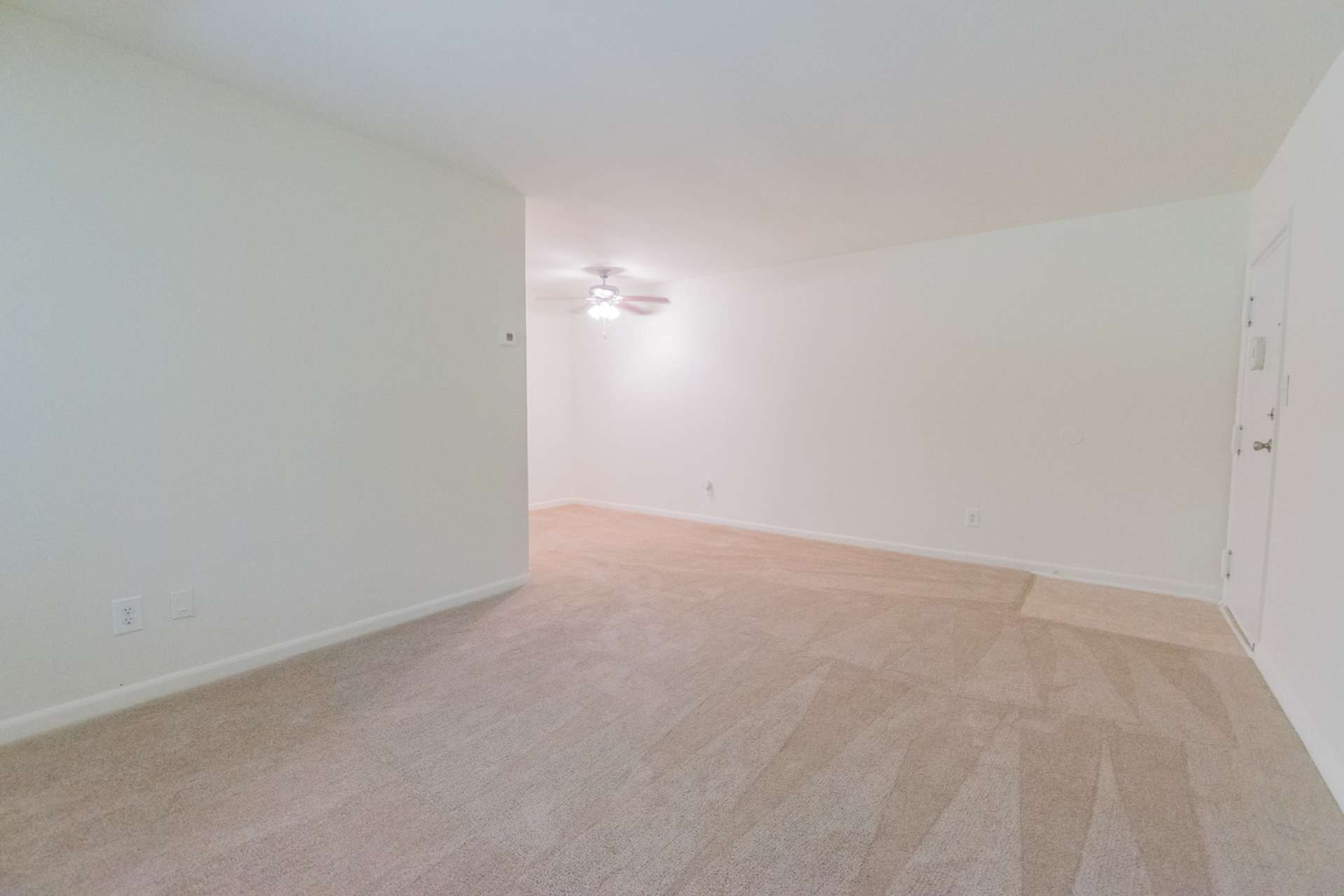 Living room area of an apartment unfurnished, fitted with carpet flooring, a ceiling fan, and a high ceiling