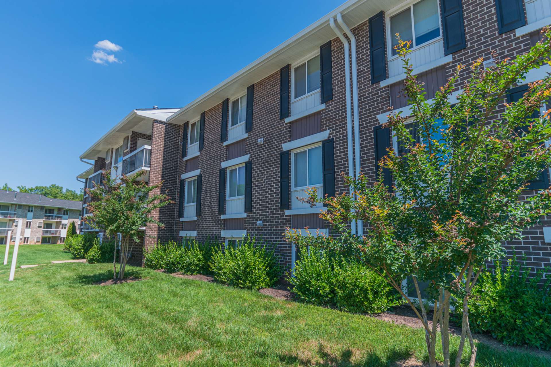 Exterior of an apartment building at Chesapeake Village apartments, fitted with paved walkway, and a lawn