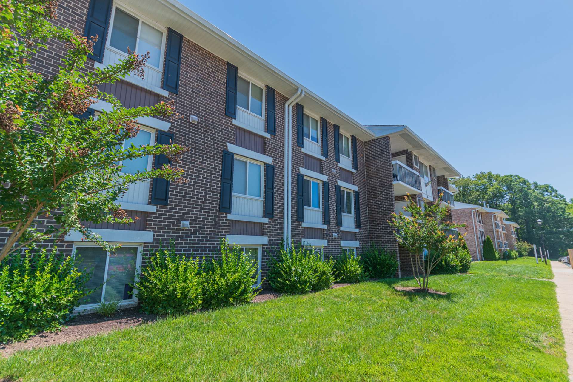 Exterior of an apartment building at Chesapeake Village apartments, fitted with paved walkway, and a lawn