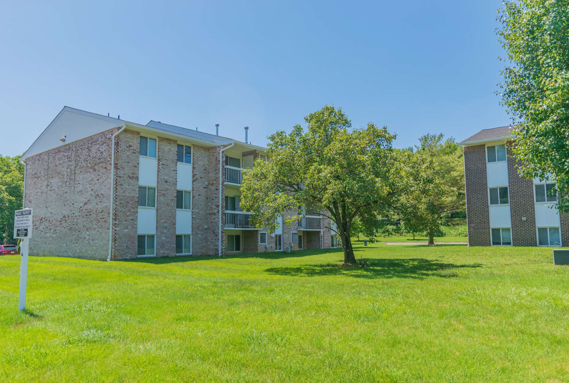 The exterior of an apartment building at Chesapeake Village apartments, fitted with a lawn, and trees