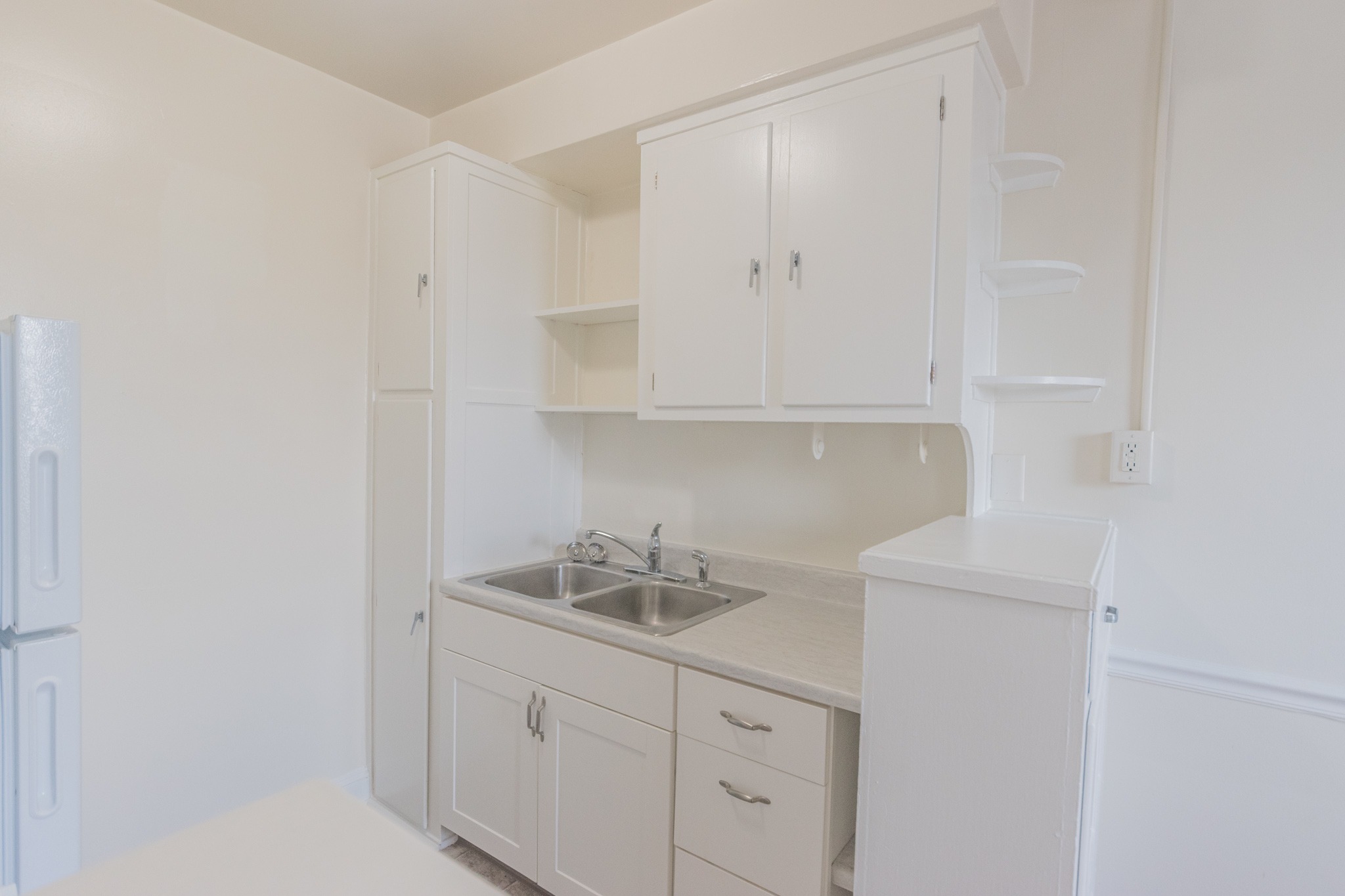 The kitchen area of an apartment, fitted with tiled flooring, spacious cabinets, and a dual sink