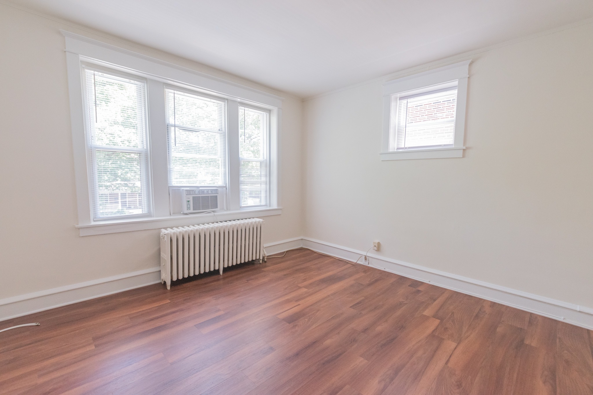 Living room area of an apartment unfurnished, fitted with vinyl flooring, a radiator, and a huge window