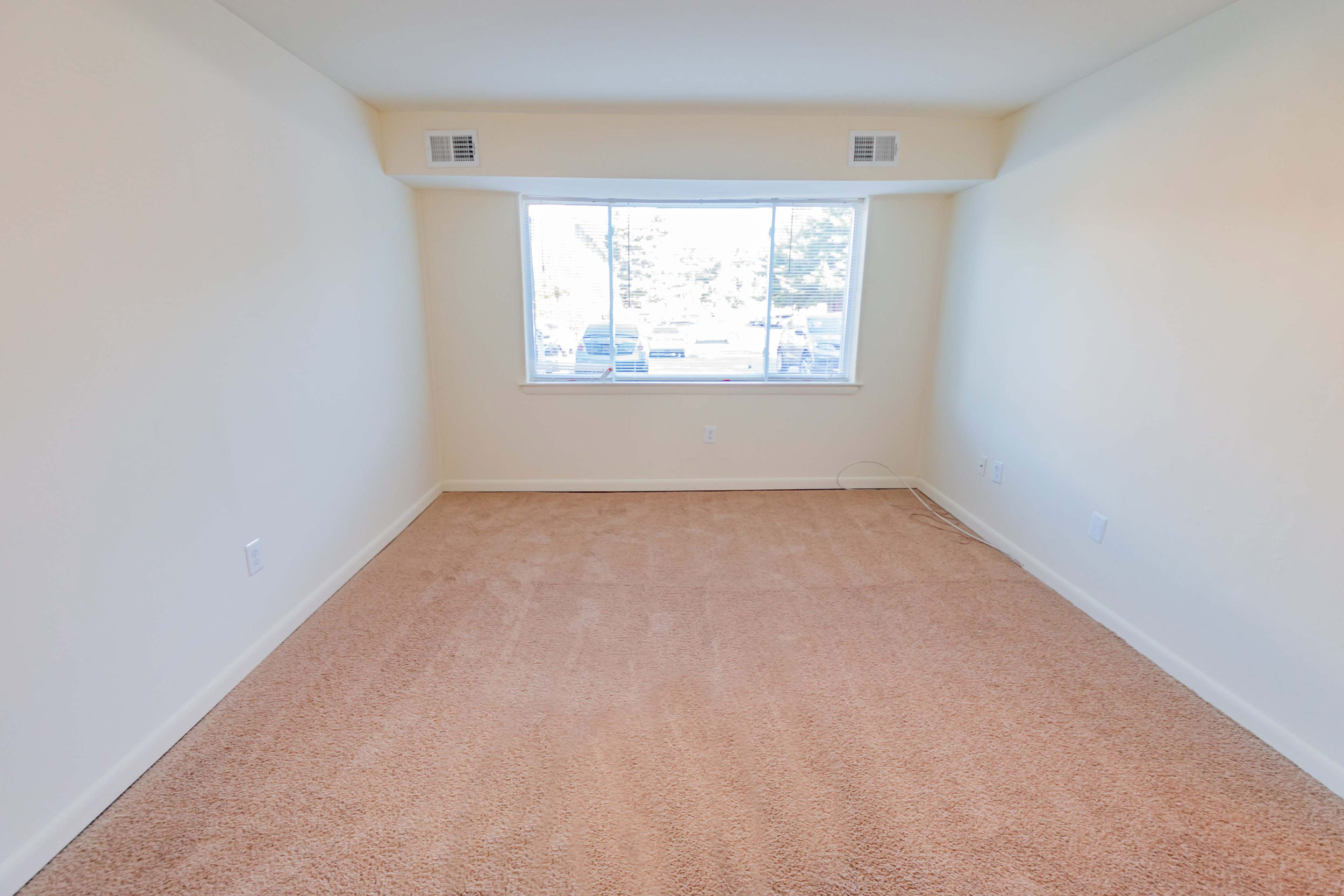 Bedroom area of an apartment unfurnished, fitted with carpet flooring, air vents, and a huge window