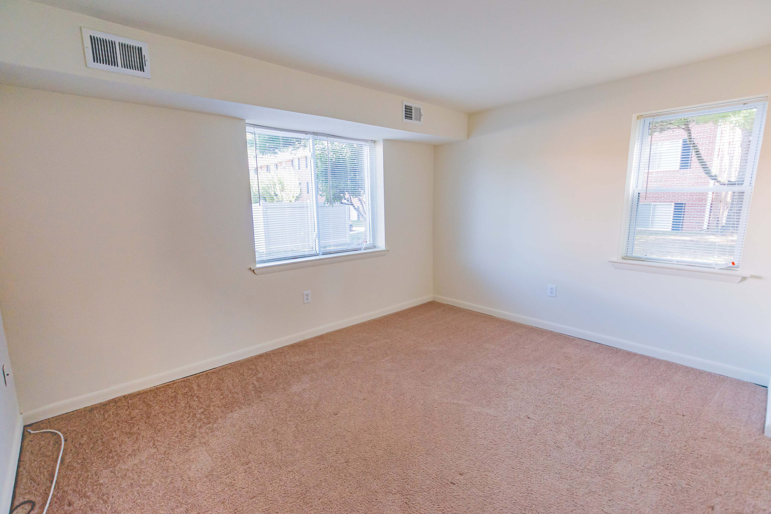 Bedroom area of an apartment unfurnished, fitted with carpet flooring, air vents, and a high ceiling