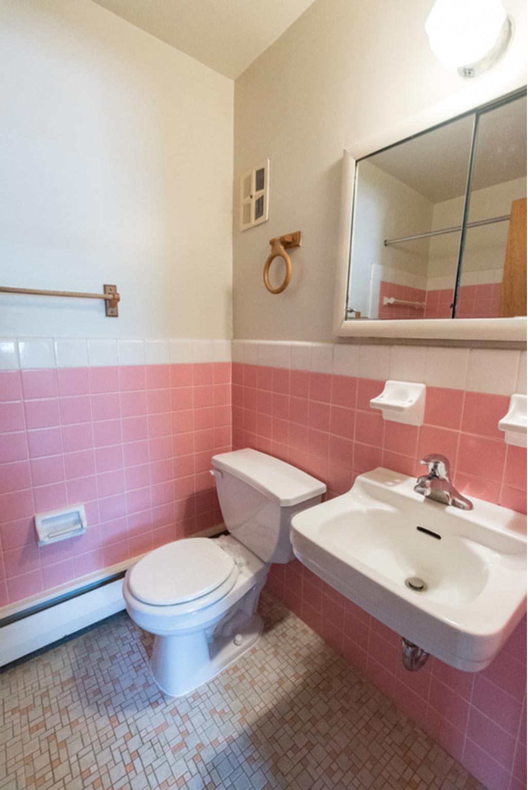 Bathroom with a mirror, light, sink, toilet, and pink tiles.