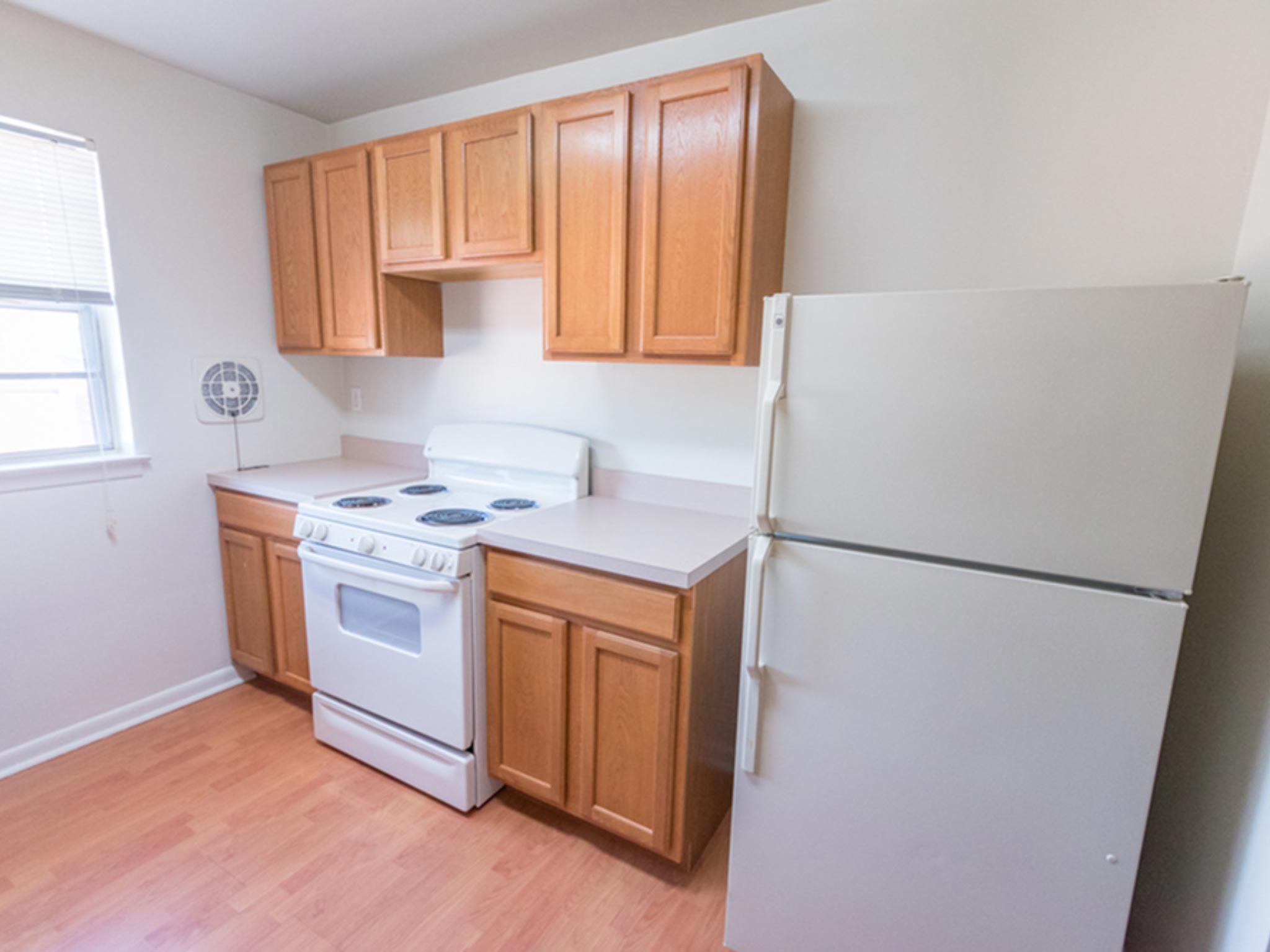 Kitchen with wooden cabinets, white appliances, and a window in Evergreen Club Apartments.