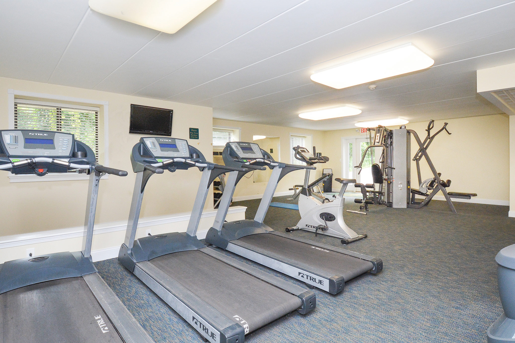 Area of our Fitness center in our community, fitted with fitness machines, soft flooring, and a high ceiling