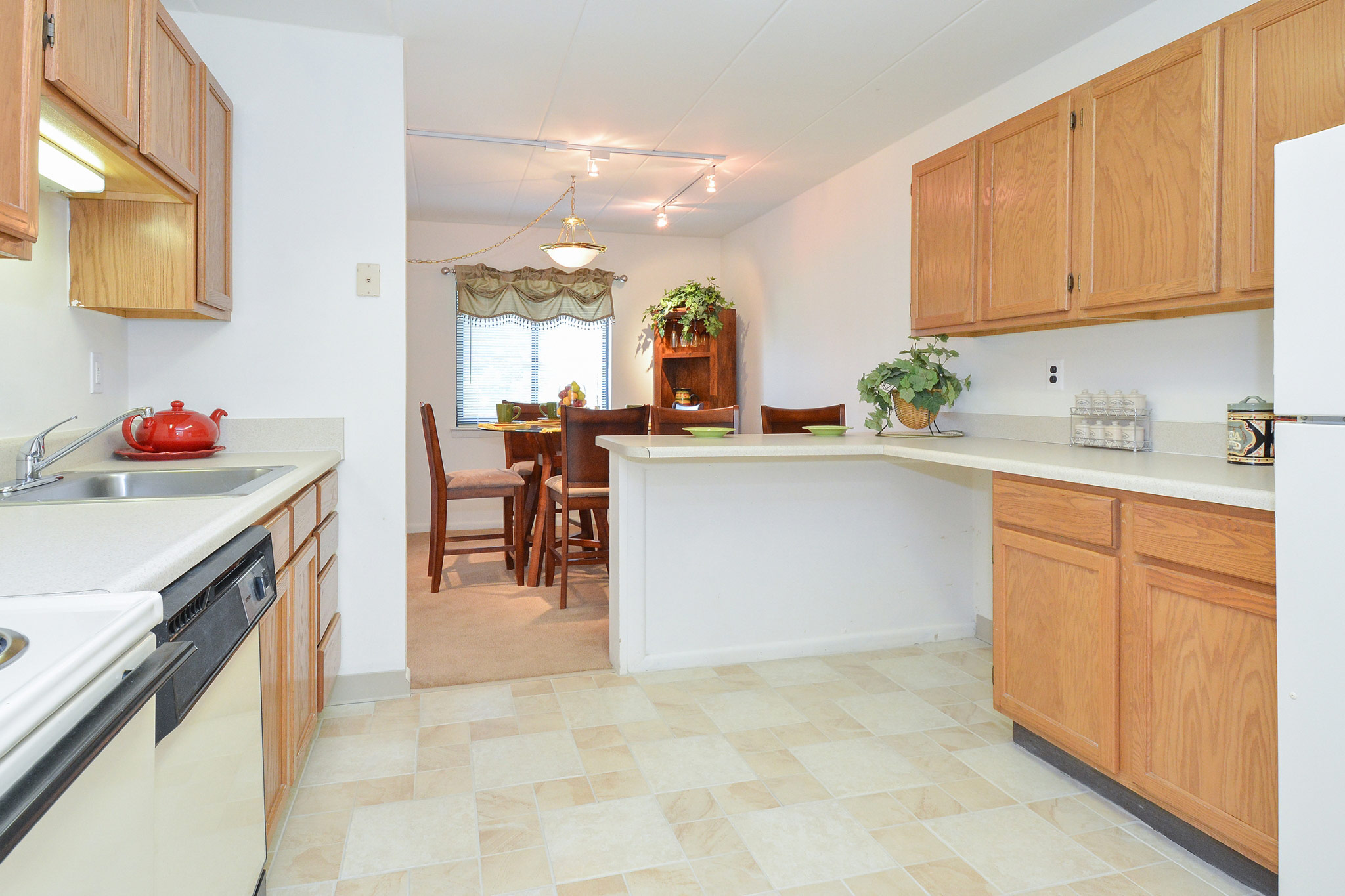 Kitchen area of an apartment, fitted with tiled flooring, a stove, a dishwasher, and a walkway to the dining area