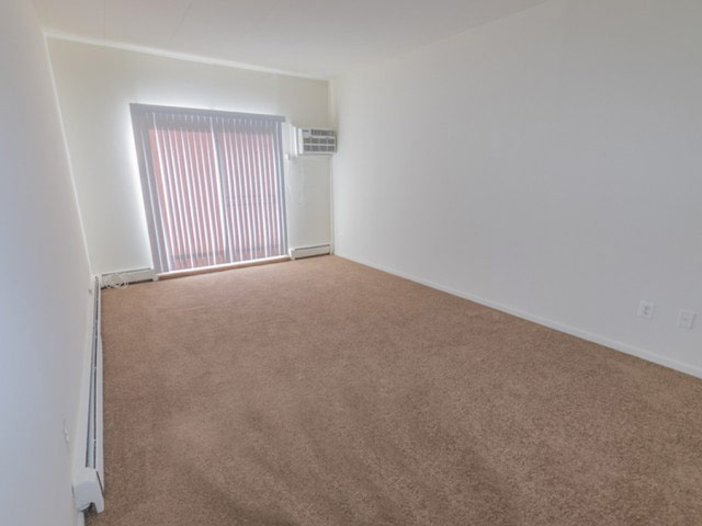 Living room area of an apartment unfurnished, fitted with carpet flooring, a high ceiling, and a sliding door