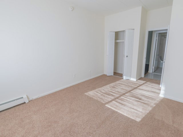 The bedroom area of an apartment unfurnished, fitted with carpet flooring, a closet, and a private bathroom area