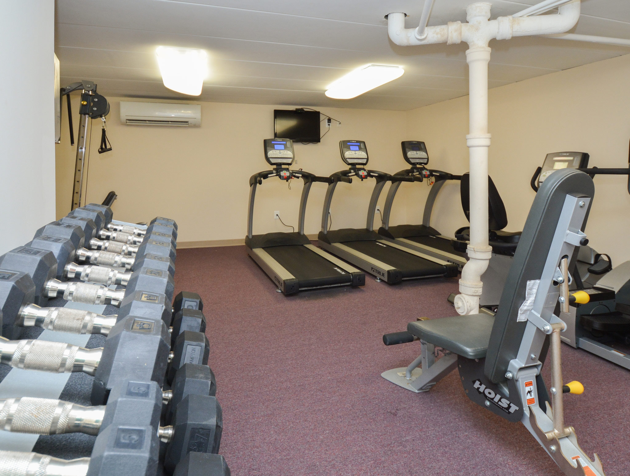 Fitness center area of our community, fitted with fitness equipment, soft flooring, and a high ceiling