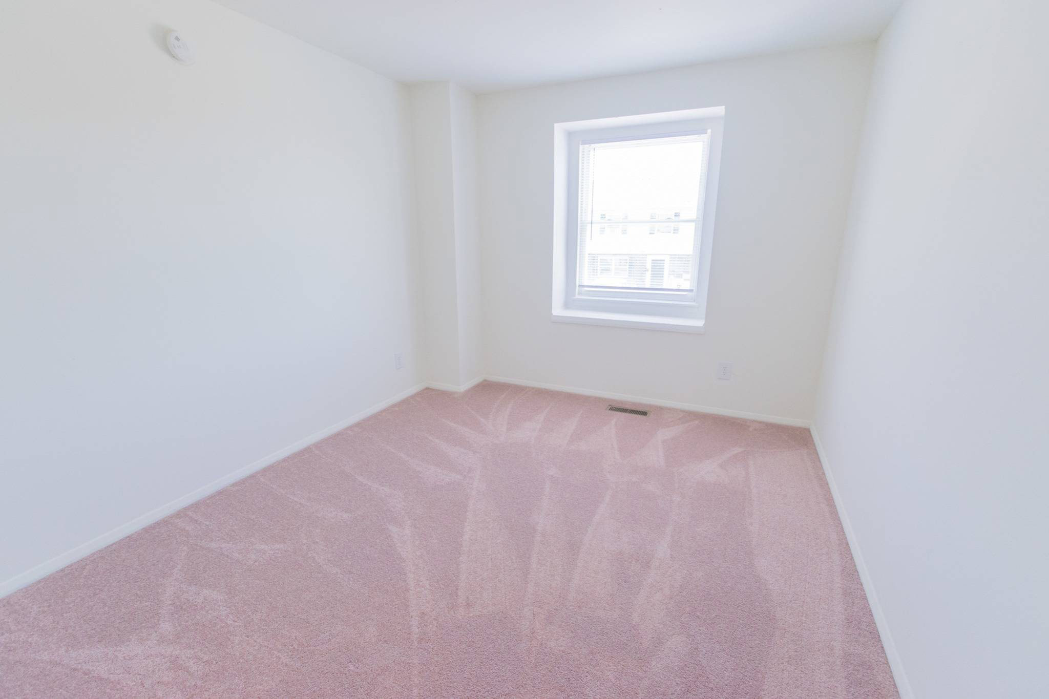 Bedroom with a window, white walls, and light pink carpet.