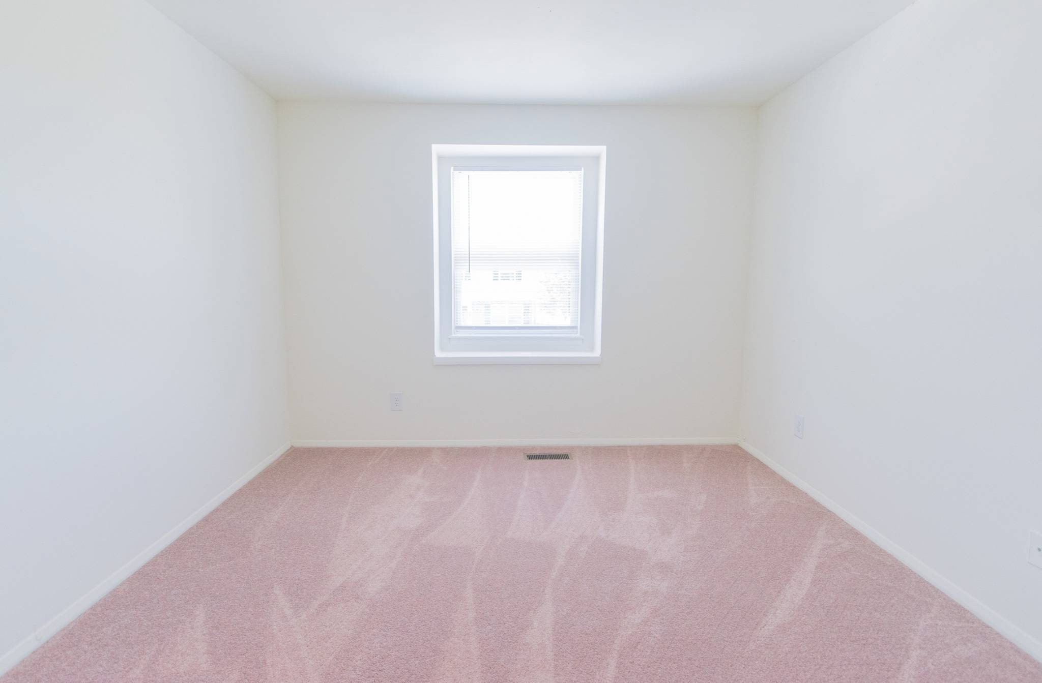Spacious bedroom with light pink carpet with a window in a bedroom at Middle River Townhomes.