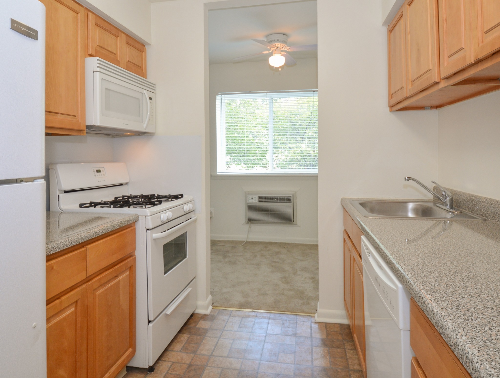 Kitchen area of an apartment, fitted with tiled flooring, spacious cabinets, a stove, a microwave, and a sink