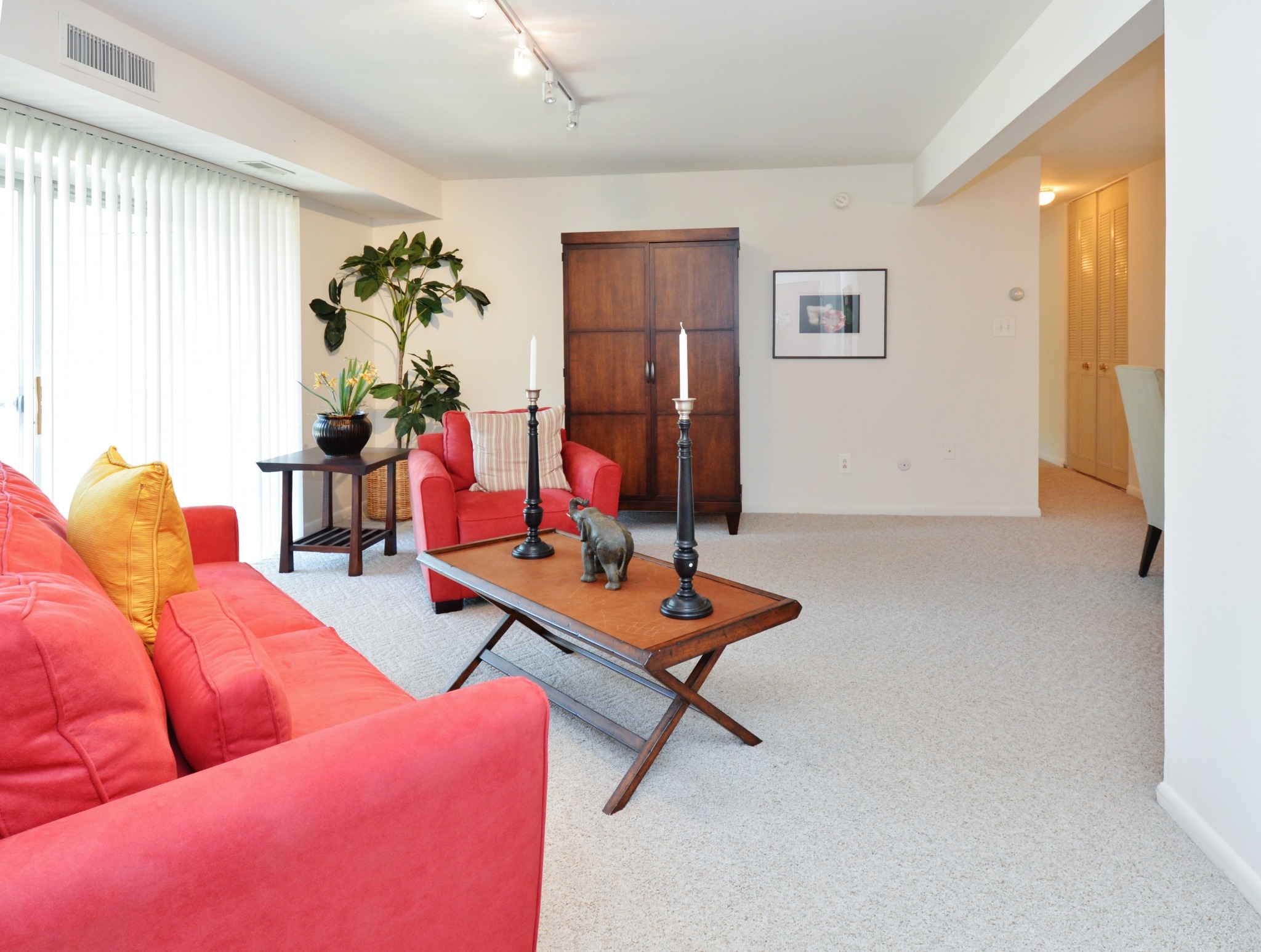 An apartment living room with a red couch, an amoire, living room table and carpeting at Valley Stream Apartments