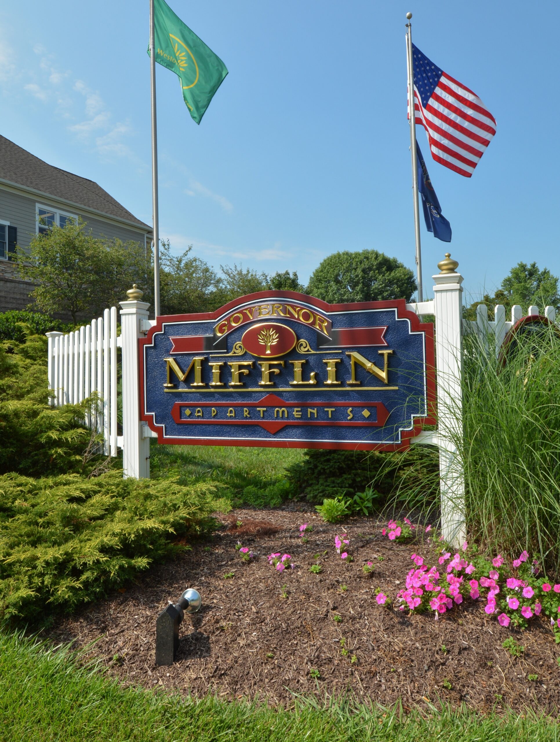 Blue and red Governor Mifflin Apartments property sign surrounded by flowers and flags