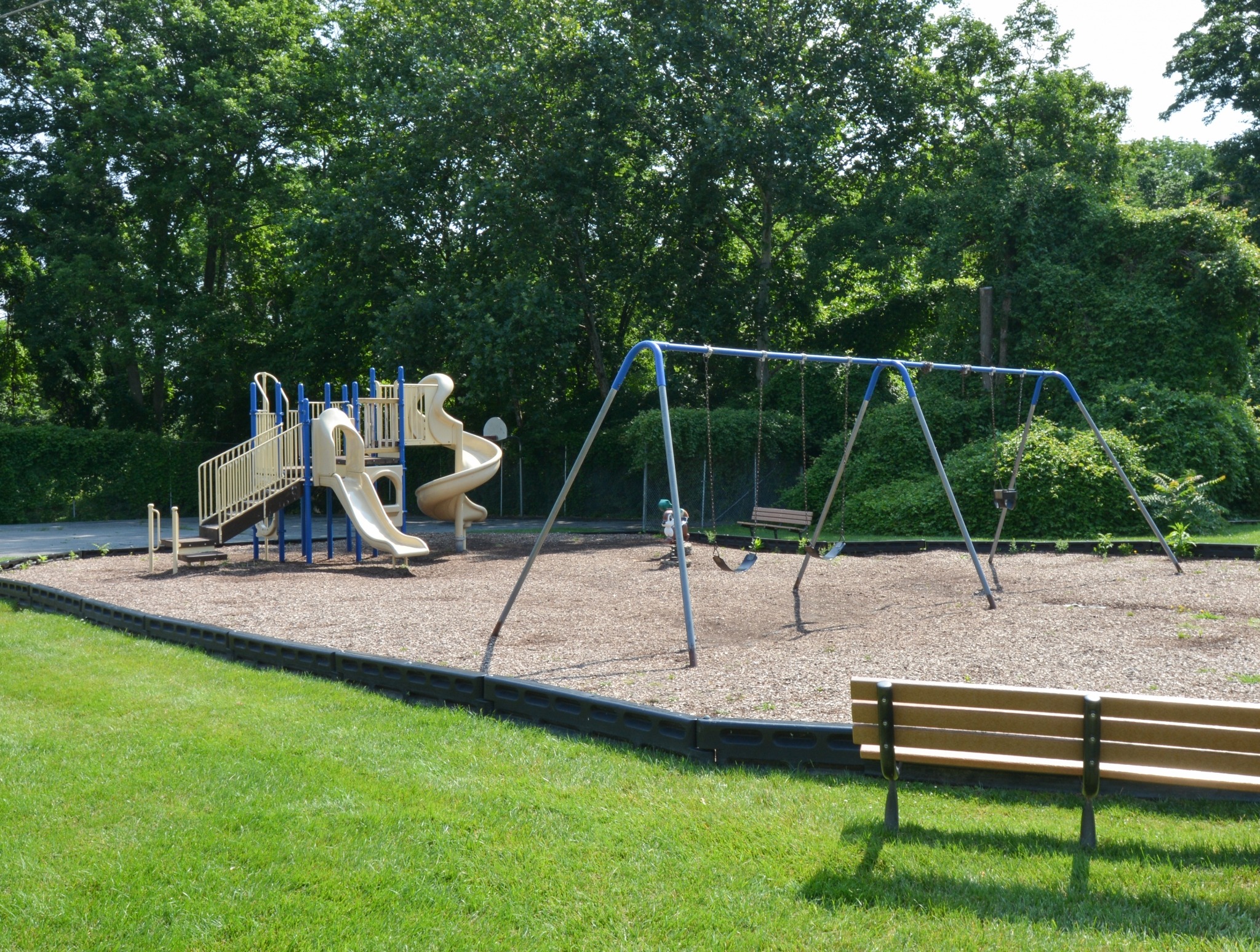 Outdoor playground on mulch surrounded by grass.