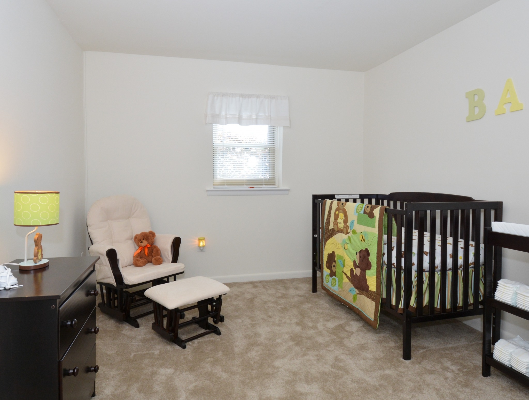 Carpeted bedroom with a crib, chair, and dresser.