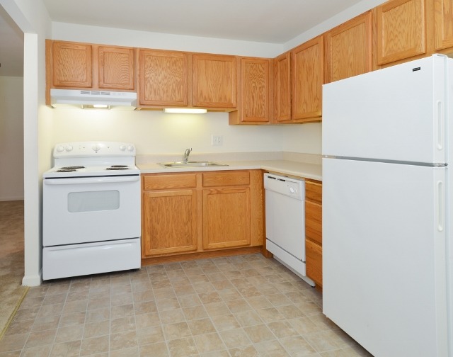 Kitchen area of an apartment, fitted with tiled flooring, spacious cabinets, a stove, and a fridge