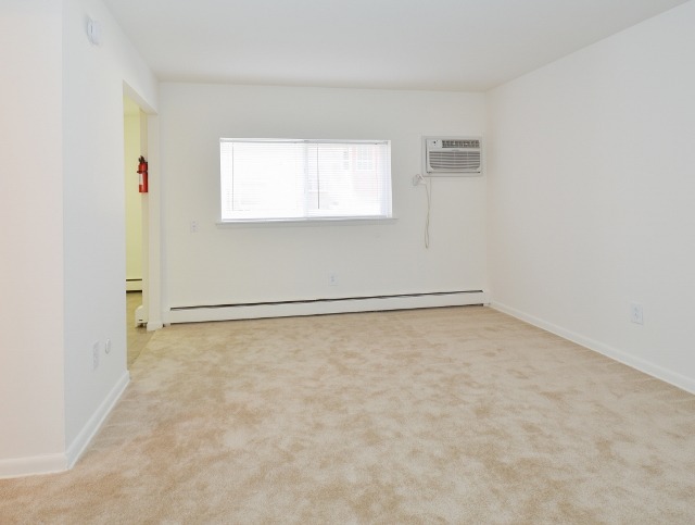 Dining area of an apartment unfurnished, fitted with carpet flooring, a huge window, and an A/C unit