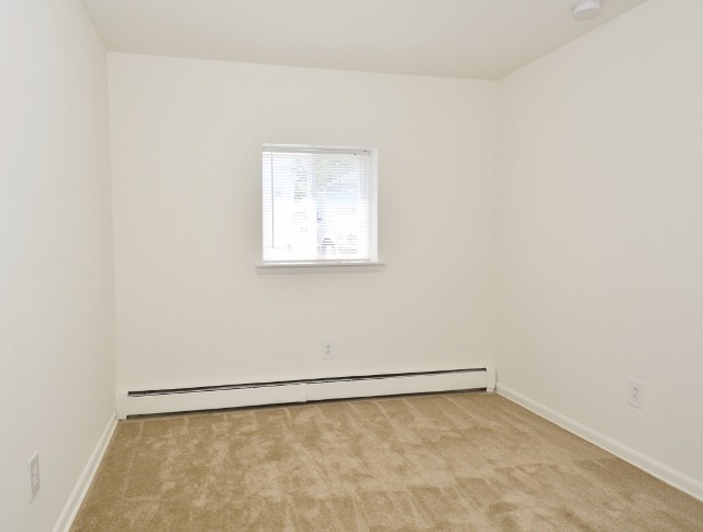Bedroom area of an apartment unfurnished, fitted with carpet flooring, huge windows, and a high ceiling