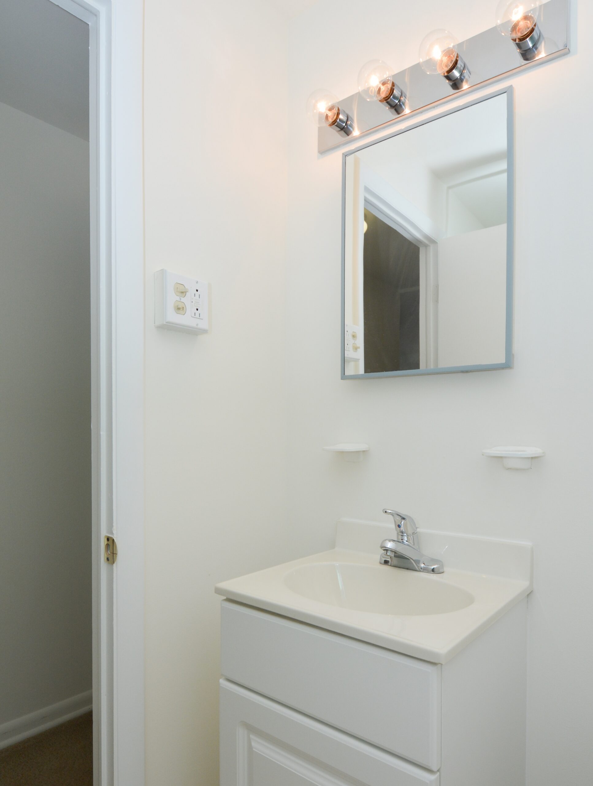 Bathroom area of an apartment fitted with a single vanity, a huge mirror, and lighting