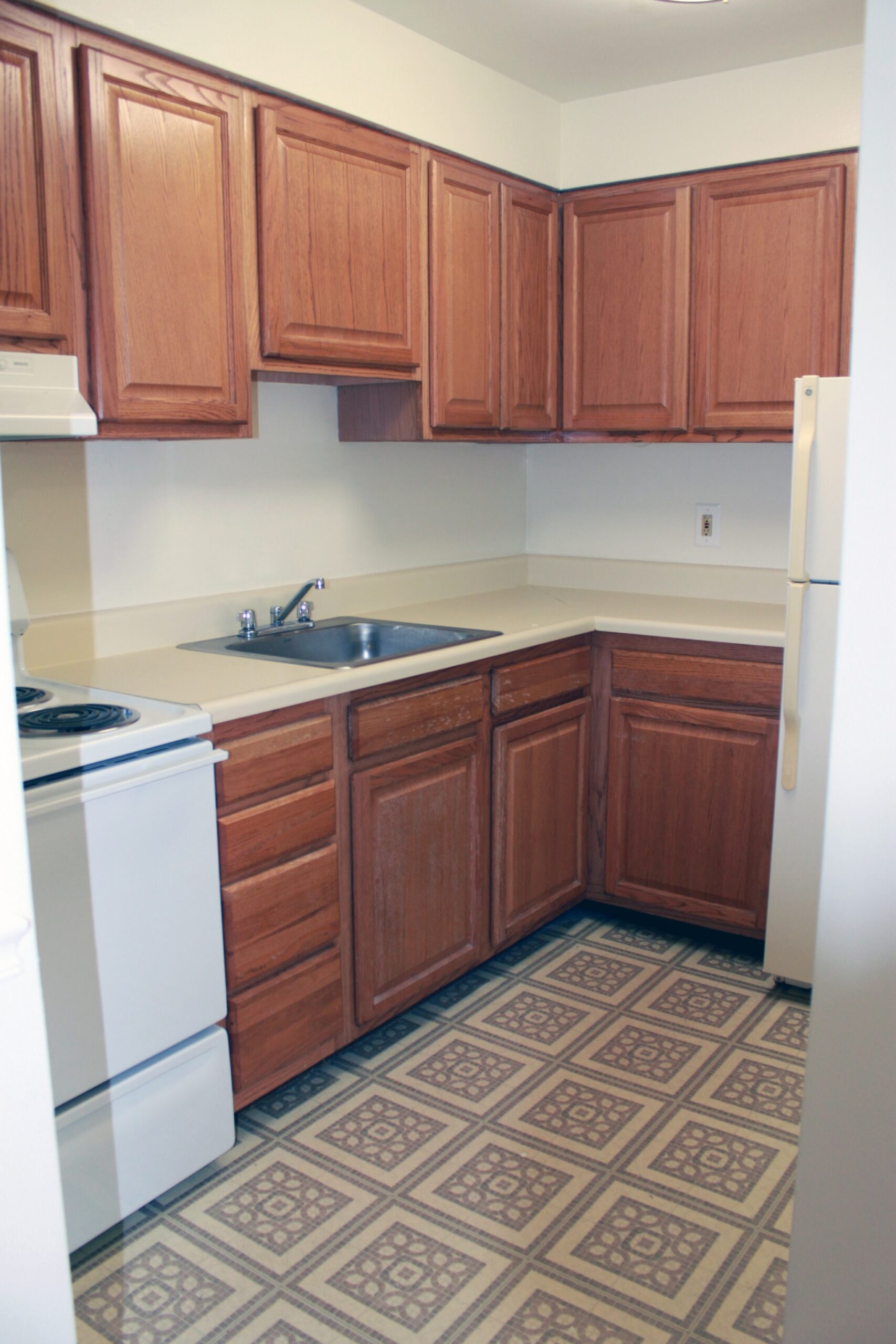 Kitchen area with wooden cabinets and white appliances in an apartment at Lansdale Village Apartments.