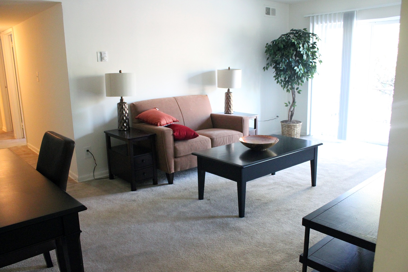 Living room area of an apartment, fitted with a couch, a coffee table, and a sliding door to patio area
