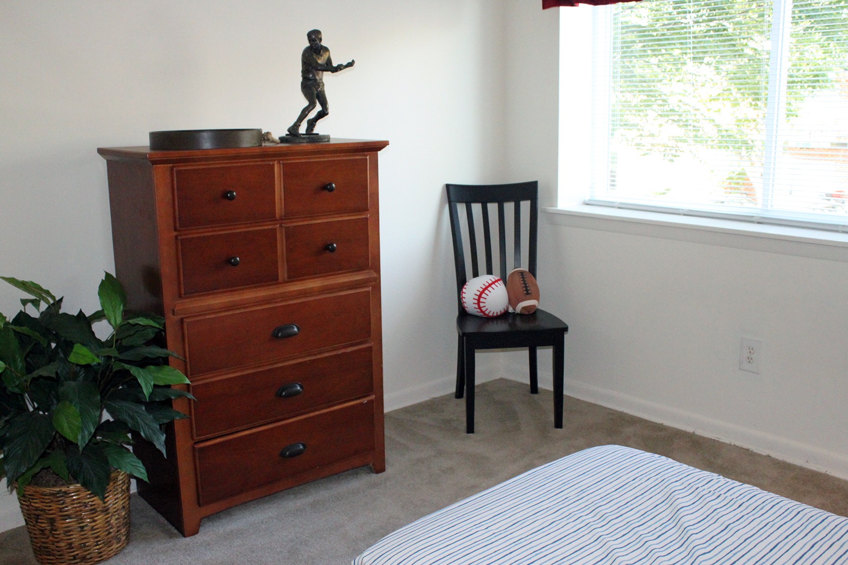 The bedroom area of an apartment, fitted with a Chester drawer, a chair, and a huge window