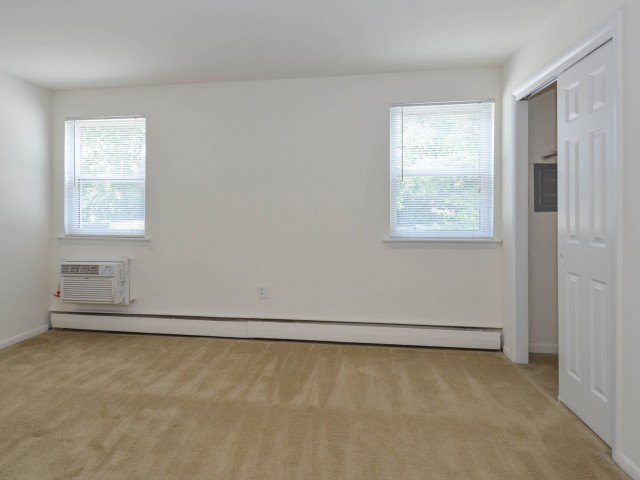 Bedroom area of an apartment unfurnished, fitted with carpet flooring, huge windows, and a walk in closet area