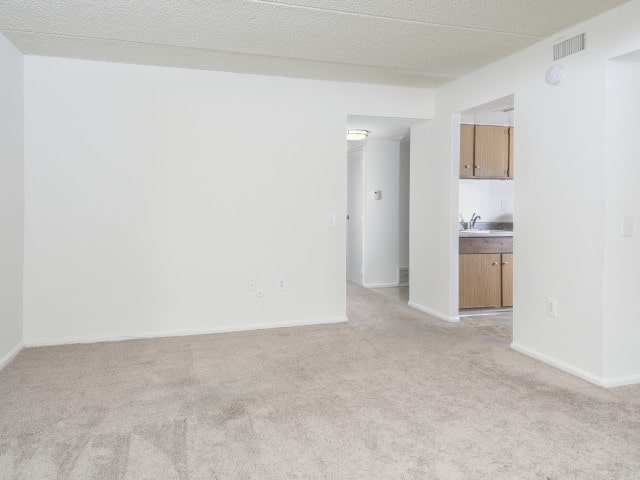 Living room area of an apartment unfurnished, fitted with carpet flooring, and a ceiling fan