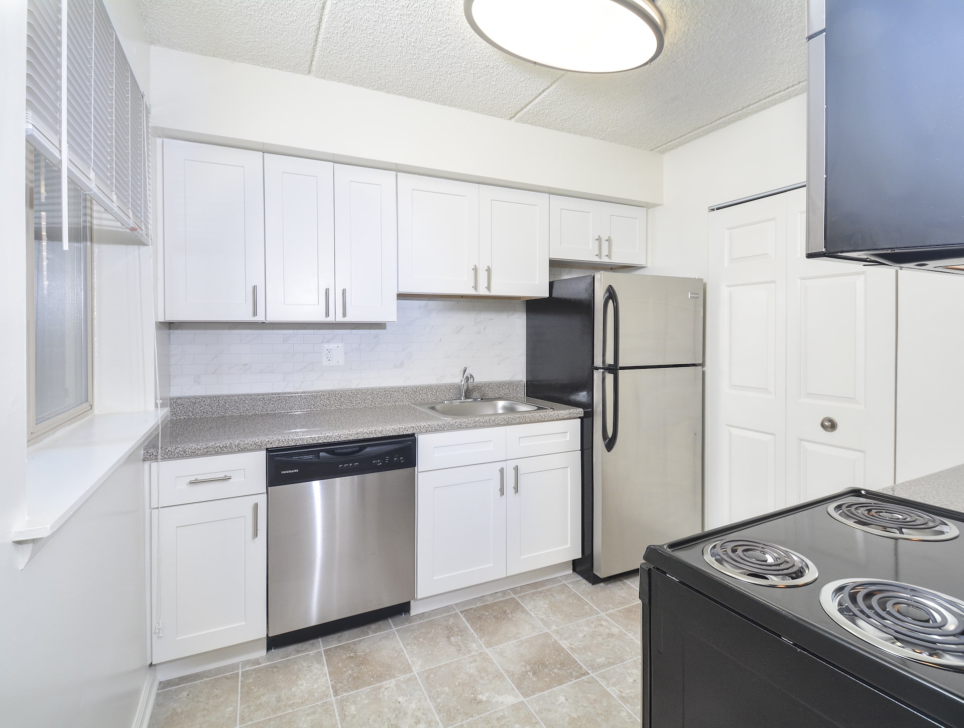 Kitchen area of an apartment, fitted with stainless steel appliances, tiled flooring, and spacious cabinets